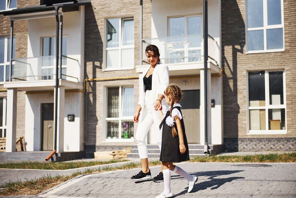 Mother and daughter in school uniforms outdoors by a building.